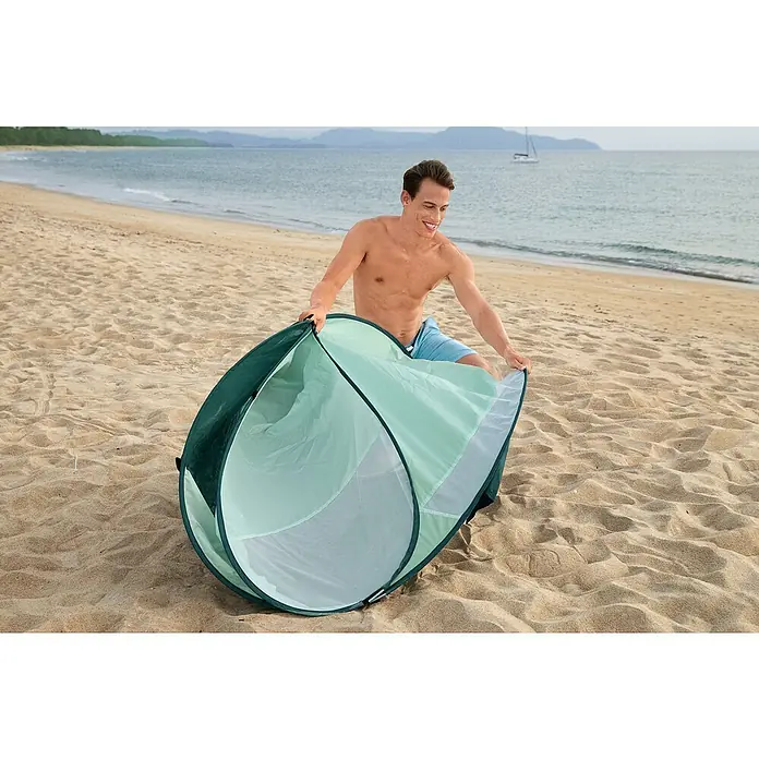 Bestway Pavillo Pop-Up StrandmuschelL x B x H: 200 x 120 x 90 cm, Türkis - Ein Mann baut am Strand eine dunkelgrüne und hellgrüne Strandmuschel auf, um sich vor der Sonne zu schützen.
