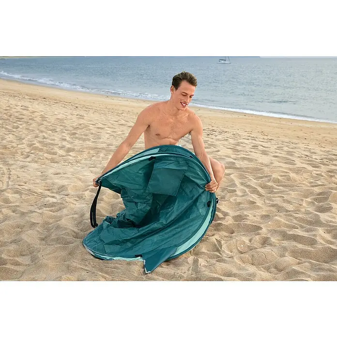 Bestway Pavillo Pop-Up StrandmuschelL x B x H: 200 x 120 x 90 cm, Türkis - Ein Mann öffnet eine türkisfarbene Strandmuschel am Strand. Das leichte, tragbare Zelt bietet Sonnenschutz und Privatsphäre für den Strandbesuch.