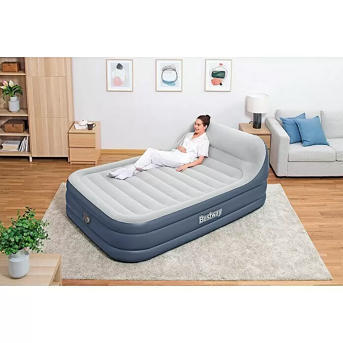 Bestway Luftbett SleekFlow - L x B x H: 226 x 152 x 84 cm, Integrierte Luftpumpe - Graue und hellgraue aufblasbare Luftmatratze mit integriertem Kopfteil, eine Frau ruht bequem darauf in einem Raum.