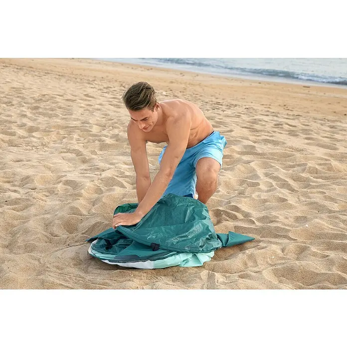 Bestway Pavillo Pop-Up StrandmuschelL x B x H: 200 x 120 x 90 cm, Türkis - Ein Mann kniet am Strand und faltet eine grüne Strandmuschel zusammen.