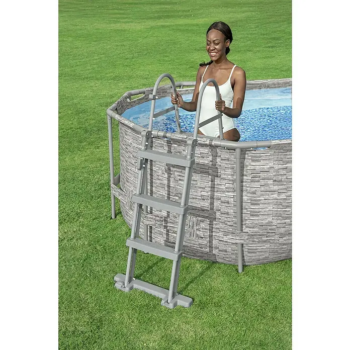 Bestway Flowclear Poolleiter - Passend für: Pools bis 107 cm Höhe, Stahl - Eine Frau steigt über eine graue Leiter in einen runden Pool mit Steinmuster ein.