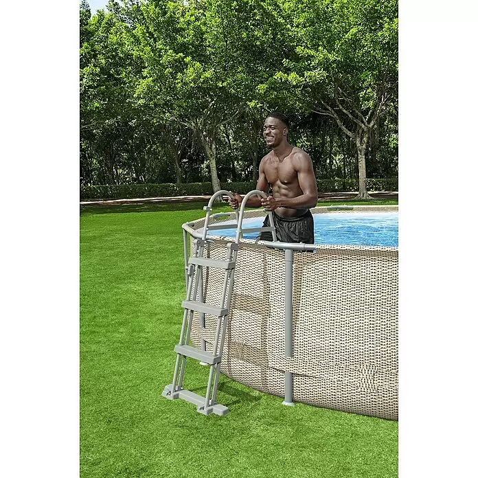 Bestway Flowclear Poolleiter - Passend für: Pools bis 107 cm Höhe, Stahl - Lächelnder Mann steigt über eine graue Leiter in einen beigefarbenen Rattan-Look Aufstellpool.