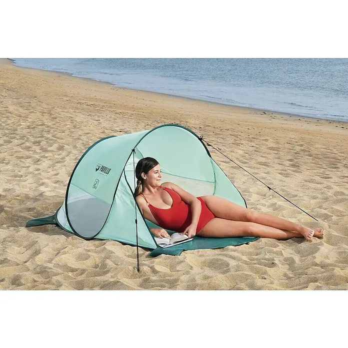 Bestway Pavillo Pop-Up StrandmuschelL x B x H: 200 x 120 x 90 cm, Türkis - Eine Frau entspannt im Pavillo Strandzelt am Strand mit einem Buch. Das Zelt bietet Schutz vor Sonne und Wind, ideal für einen entspannten Tag.