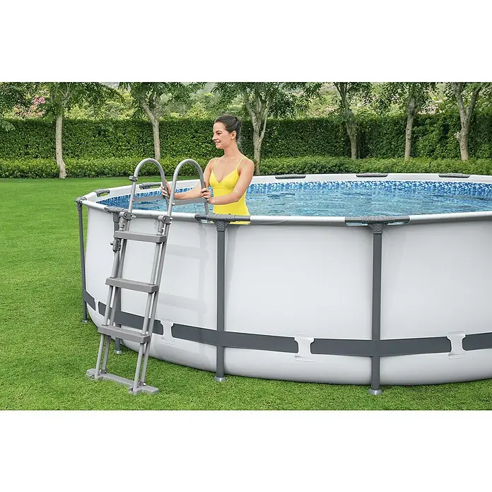 Bestway Frame-Pool Steel Pro Max - Ø x H: 366 x 100 cm, Lichtgrau, 9.150 l - Frau steigt mit einer Leiter in einen runden, oberirdischen Pool. Der Pool ist aus weißem Vinyl gefertigt und hat einen grauen Rahmen.
