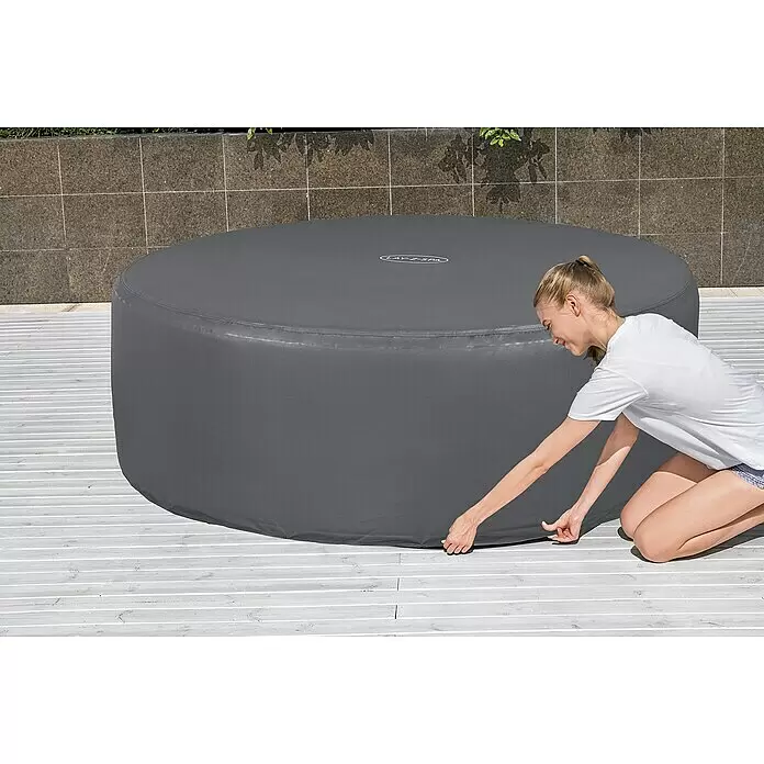 Bestway Lay-Z-Spa Pool-Abdeckplane - Passend für: Runde Whirlpools bis Ø x H: 196 x 71 cm - Frau befestigt eine graue runde aufblasbare Whirlpoolabdeckung mit 'LAY-Z-SPA'-Logo auf einer Terrasse.