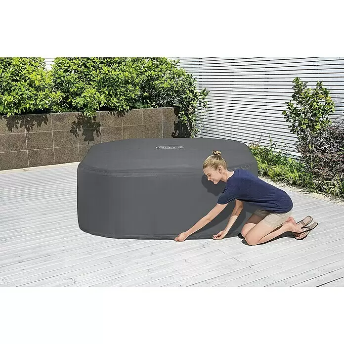 Bestway Lay-Z-Spa Pool-Abdeckplane - Passend für: Quadratische Whirlpools bis L x B x H: 180 x 180 x 71 cm, L x B x H: 180 x 180 x 71 cm - Frau deckt grauen aufblasbaren Lay-Z-Spa Whirlpool auf einer Terrasse ab.