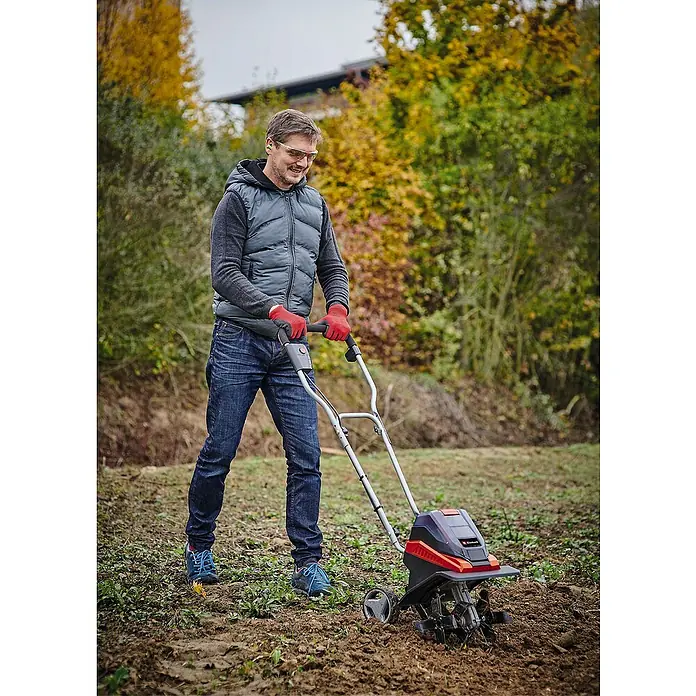 Einhell Power X-Change 18V Akku-Bodenhacke GE-CR 30 Li-Solo - Anzahl Akkus: Ohne Akku, Li-Ionen - Ein Mann benutzt eine Elektrohacke im Garten. Die Elektrohacke ist rot und schwarz und der Mann trägt Handschuhe und eine Schutzbrille.