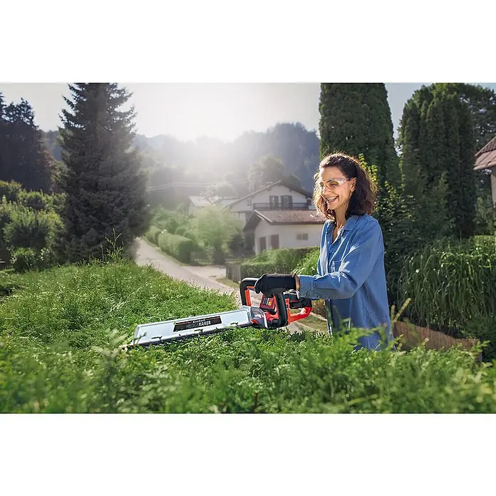 Einhell Power X-Change 18V Akku-Heckenschere Arcurra 18/55 - 18 V, Li-Ionen, Ohne Akku, Schnittlänge: 55 cm - Frau arbeitet im Garten mit einer Einhell Heckenschere mit dem Namen Einhell Hedge Raker und trägt dabei eine Schutzbrille und Handschuhe.