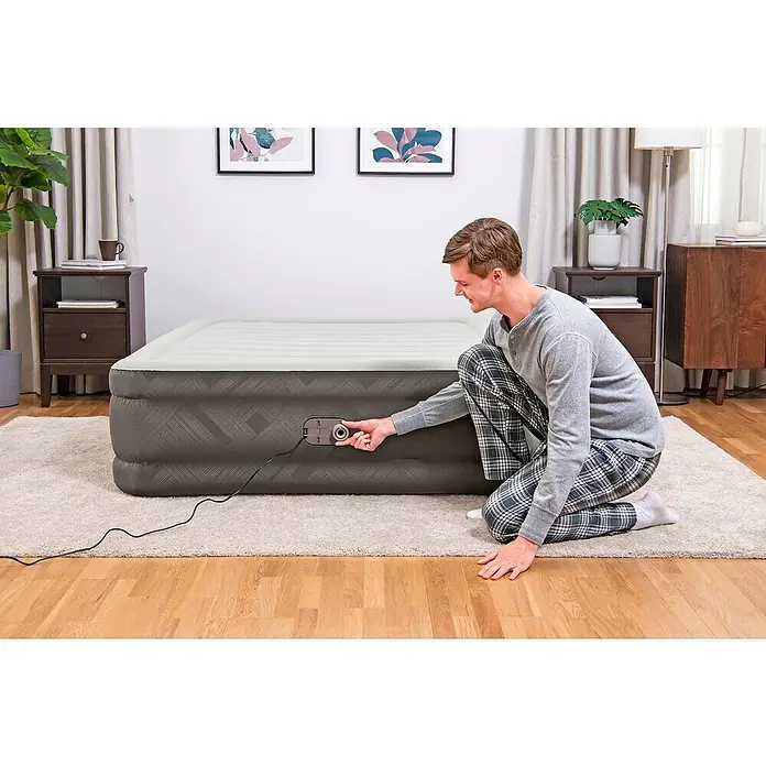 Bestway Luftbett Fortech - L x B x H: 203 x 152 x 46 cm, Integrierte Luftpumpe - Ein Mann in Schlafanzug pumpt eine graue Luftmatratze mit integrierter Pumpe in einem Schlafzimmer auf.