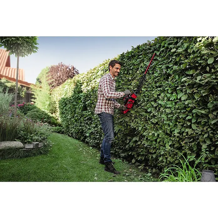 Einhell Power X-Change 18V Akku-Heckenschere GE-CH 36/65 Li-Solo - 36 V, Ohne Akku, Schnittlänge: 65 cm - Ein Mann schneidet eine Hecke mit einer roten Heckenschere in einem gepflegten Garten.