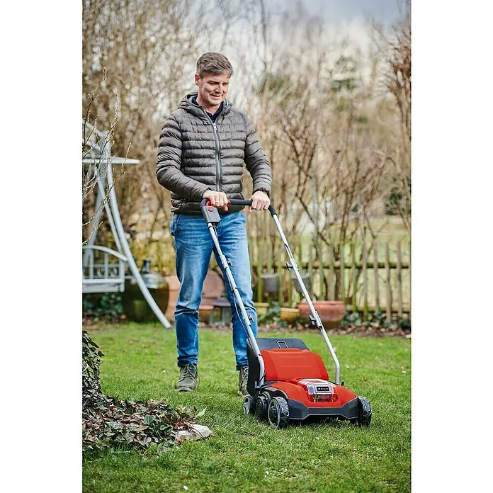 Einhell Power X-Change 18V Akku-Vertikutierer-Lüfter GC-SC 18/28 LI-SOLO - Anzahl Akkus: Ohne Akku, 18 V, Arbeitsbreite: 28 cm - Ein Mann benutzt einen Einhell Rasenlüfter im Garten, um den Rasen zu pflegen. Der Rasenlüfter ist rot und schwarz.