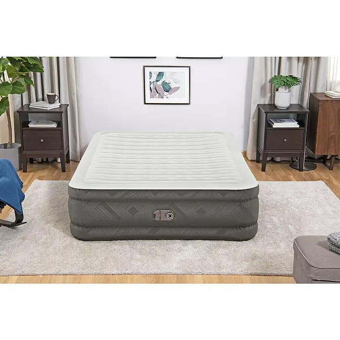 Bestway Luftbett Fortech - L x B x H: 203 x 152 x 46 cm, Integrierte Luftpumpe - Nahaufnahme einer grauen und weißen Luftmatratze, die auf einem Teppich in einem Schlafzimmer mit Nachttischen und Dekoration steht.