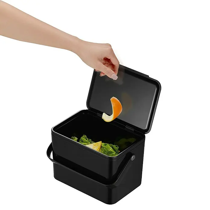 Vepa Bins Standard Mülleimer Foodwaste Caddy - 4 l, Kunststoff, Schwarz - Ein schwarzer Komposteimer wird mit einer Hand geöffnet, die eine Orangenschale hineinwirft. Praktisch für Küchenabfälle.
