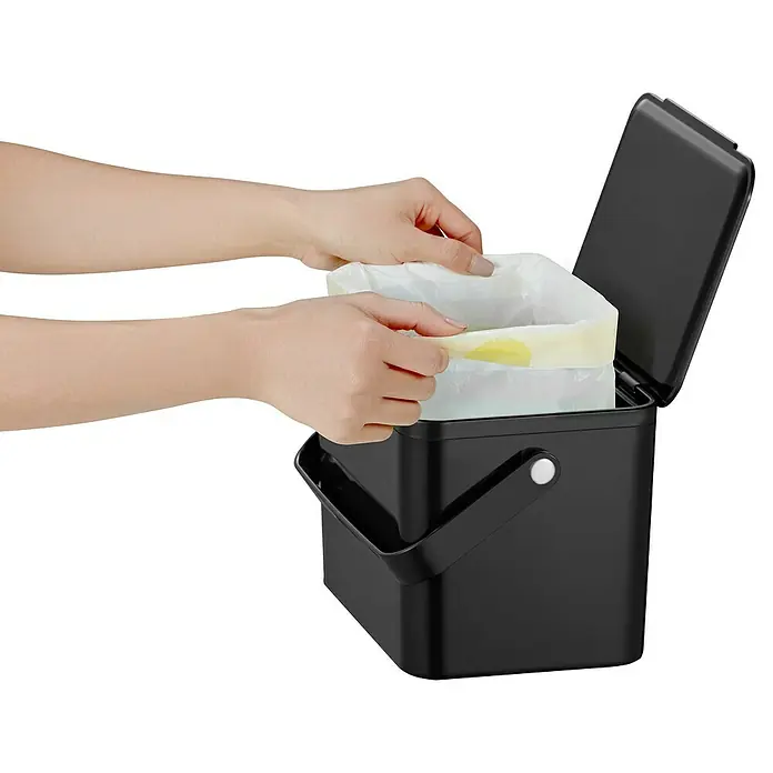 Vepa Bins Standard Mülleimer Foodwaste Caddy - 4 l, Kunststoff, Schwarz - Hier ist ein schwarzer Komposteimer mit einem weißen Beutel, der von Händen gehalten wird. Der Deckel ist geöffnet.