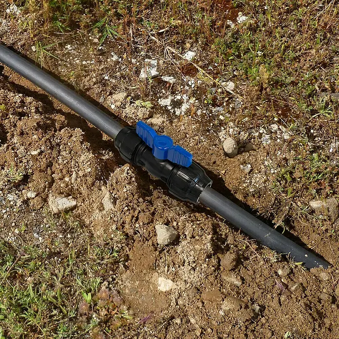 Válvula esférica PE para riego - Diámetro: 32 mm, Polietileno - Primer plano de una manguera de riego negra con una válvula de cierre azul colocada sobre tierra. La válvula es el elemento central de la imagen.