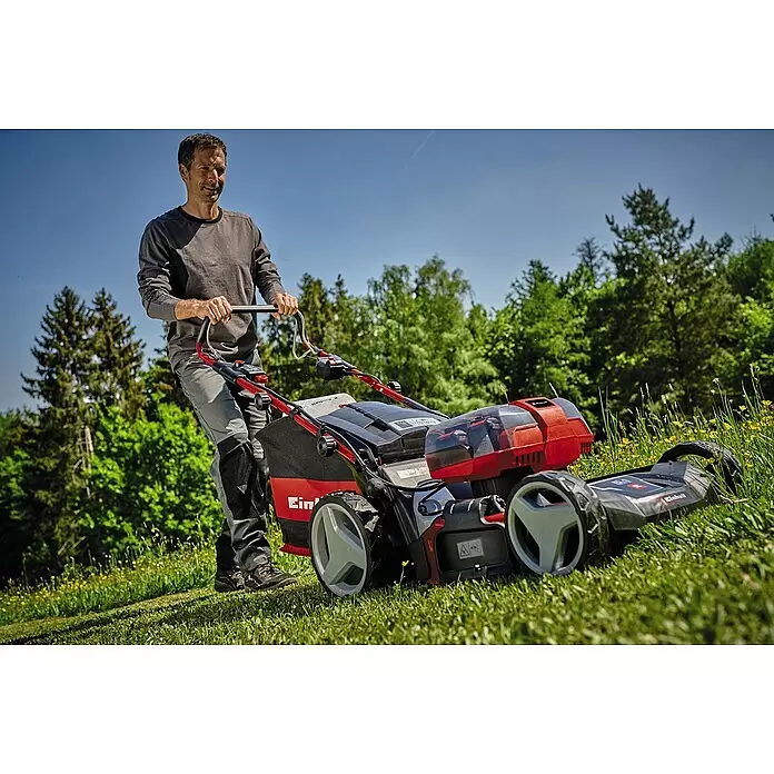 Einhell Professional Akku-Rasenmäher GP-CM 36/47 S HW Li - 18 V, 4 Akkus, 4 Ah, Schnittbreite: 47 cm - Mann bedient einen rot-schwarzen Einhell Rasenmäher auf grünem Rasen unter blauem Himmel.