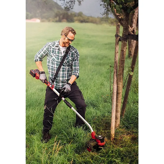 Einhell Power X-Change 18V Akku-Rasentrimmer GE-CT 36/30 Li E-Solo - 36 V, Ohne Akku - Ein Mann benutzt einen Rasentrimmer, um Gras um Bäume herum zu trimmen. Das Gerät ist rot und silberfarben.