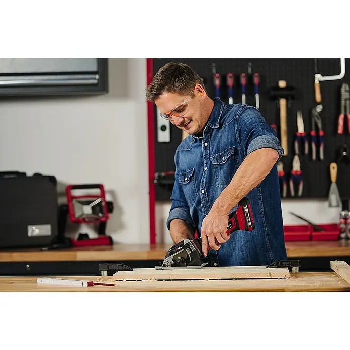 Einhell Power X-Change 18V Akku-Handkreissäge TE-CS 18/89Li-Solo - 18 V, Ohne Akku, Leerlaufdrehzahl: 0 U/min - 2.500 U/min - Ein Mann benutzt eine Einhell Akku-Handkreissäge zum Zuschneiden eines Holzbretts, wobei er Schutzbrille und Ohrenstöpsel trägt.