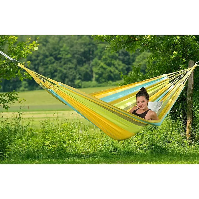 Amazonas Doppelhängematte Colombiana - L x B: 350 x 160 cm, Limona - Eine junge Frau entspannt in einer bunten Hängematte im Garten, umgeben von üppigem Grün. Die Hängematte bietet Komfort und Entspannung im Freien.