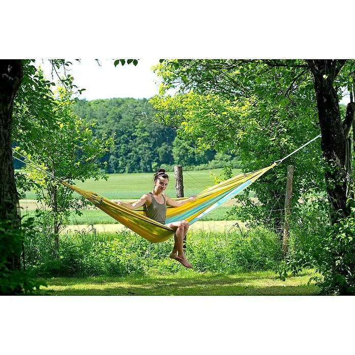 Amazonas Doppelhängematte Colombiana - L x B: 350 x 160 cm, Limona - Frau entspannt in einer bunten Hängematte zwischen Bäumen. Ideal für Garten, Terrasse oder Camping, um die Natur zu genießen.