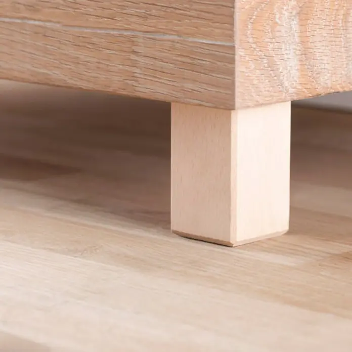 Rei Pata para muebles - L x An x Al: 5 x 5 x 8 cm, Capacidad de carga: 20 kg, Madera - Primer plano de una pata de mueble de madera clara sujeta a un mueble sobre un piso de madera, mostrando un diseño moderno.