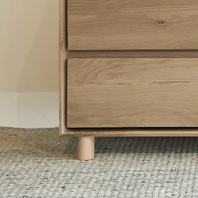 Rei Pata para muebles - L x An x Al: 6,5 x 6,5 x 8 cm, Capacidad de carga: 20 kg, Madera - Primer plano de un mueble de madera con cajones, destacando la veta natural y las patas cilíndricas sobre una alfombra texturizada.