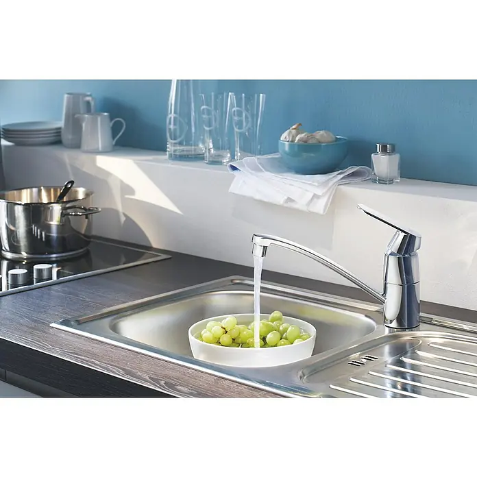 Grohe Eurosmart Cosmopolitan Spültischarmatur - Chrom, Glänzend - Nahaufnahme einer modernen Küchenarmatur über einer Spüle mit einer Schale grüner Trauben, die unter fließendem Wasser gereinigt werden.