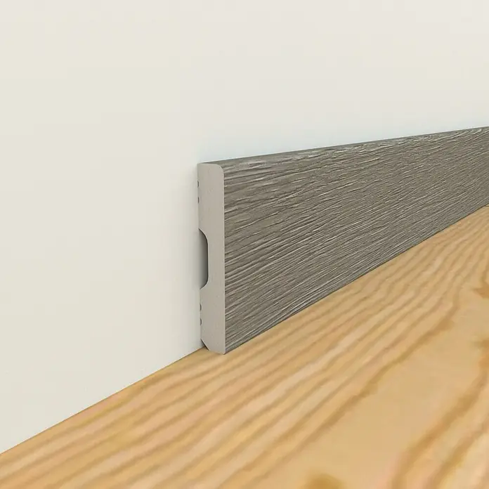 Oknum Rodapié Aneto - 200 cm x 14 mm x 90 mm - Un primer plano de un zócalo gris con textura de grano de madera, instalado contra una pared blanca sobre un piso de madera clara.