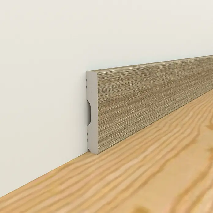 Oknum Rodapié Cervino - 200 cm x 14 mm x 90 mm - Un primer plano muestra un zócalo con aspecto de madera elegantemente instalado contra una pared blanca y un piso de madera, realzando la estética.