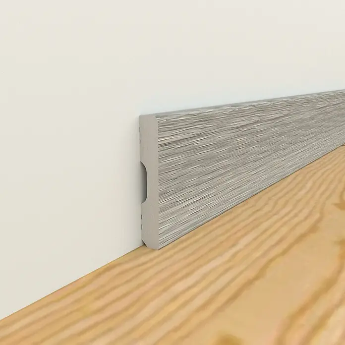 Oknum Rodapié Veleta - 200 cm x 14 mm x 90 mm - Primer plano de un zócalo gris con veta de madera, instalado contra una pared blanca y un suelo de madera clara.