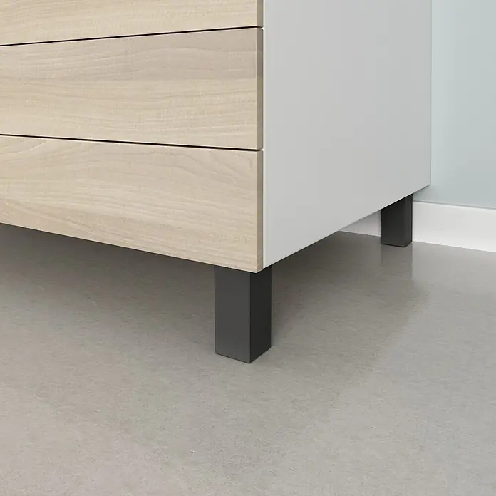 Rei Möbelfuß - L x B x H: 4 x 8 x 10 cm, Kunststoff, Schwarz, 1 Stk. - Nahaufnahme eines modernen, hellen Holzkommode mit schlichten, dunklen Metallfüßen auf einem grauen Boden.