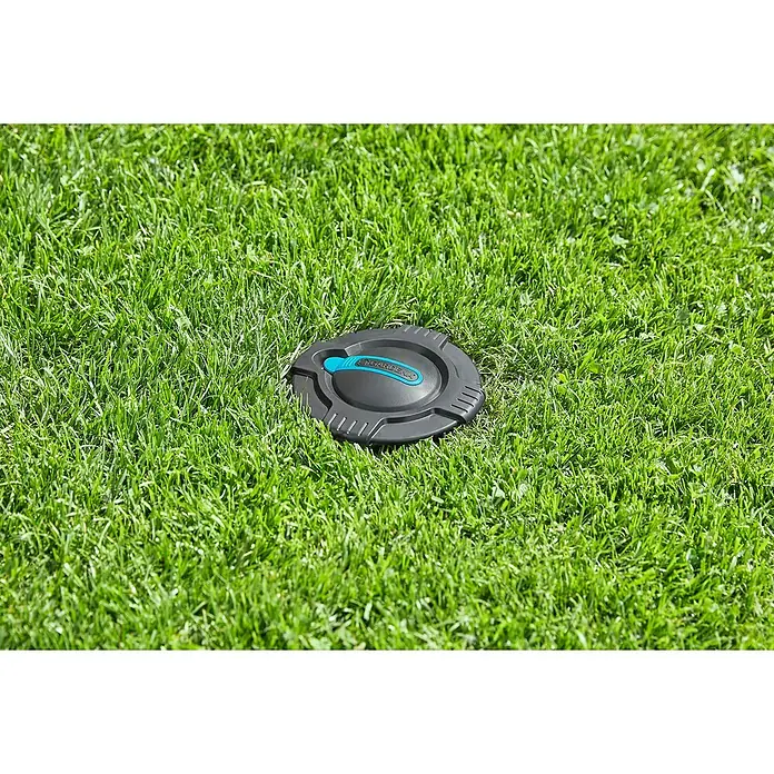 Gardena Sprinklersystem Wassersteckdose - ¾″ - Nahaufnahme einer grauen GARDENA-Bewässerungsdose mit blauem Akzent inmitten üppigen, grünen Grases, ideal für Gartenbewässerung.