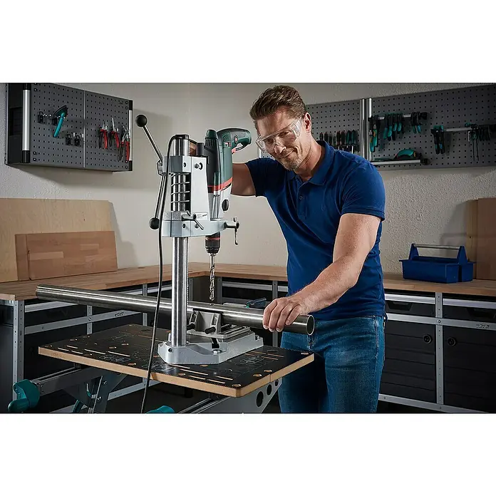 Wolfcraft Soporte de taladro - L x An x Al: 307 x 203 x 570 mm, Apertura máxima: 60 mm - Un hombre usa un taladro de columna Wolfcraft para perforar una tubería de metal. ¡La ropa de trabajo segura es importante!