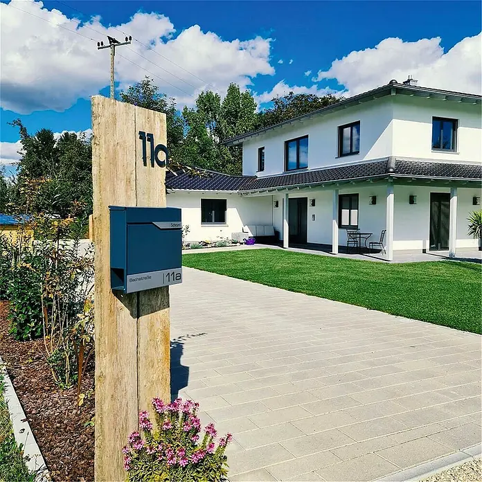 Metzler Wandbriefkasten Siebert - L x B x H: 8,5 x 37 x 35,5 cm, Anthrazit, Stahl, Zeitungsfach - Elegante blaue Briefkastenanlage auf Holzpfosten vor einem modernen Haus, die stilvolle Funktionalität vereint.