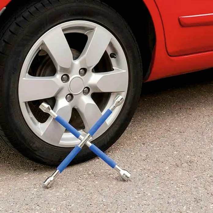 Goodyear Llave fija de tubo en cruz - Sencillo, Ancho de llave: 17 mm - 22 mm - Una llave de cruz con mangos azules está tirada delante de un neumático. La herramienta está lista para cambiar la llanta del auto rojo.
