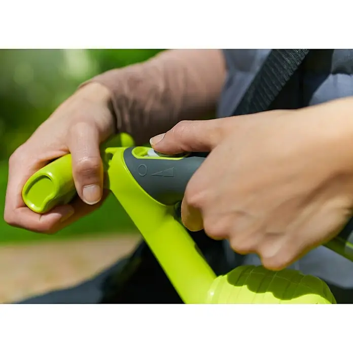 Ryobi Elektro-Laubbläser RBV3000CSV - 3.000 W, Blasgeschwindigkeit: 375 km/h, Blasleistung: 14 m³/min - Nahaufnahme einer Person, die einen gelb-grauen Trimmer bedient. Hervorgehoben werden Griff und Bedienungselemente des Geräts.