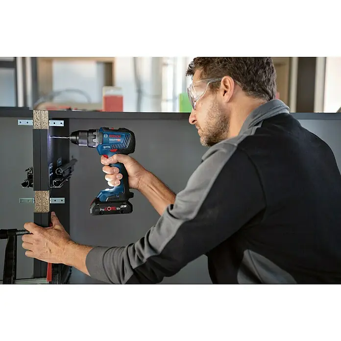 Bosch Professional AMPShare 18V Akku-Bohrschrauber GSR 18V-55 - 18 V, 2 Akkus, 4 Ah - Ein Handwerker benutzt einen Bosch Professional Akku-Bohrschrauber, um an einem Möbelstück zu arbeiten. Die Bohrmaschine ist blau und hat einen 18V Akku.