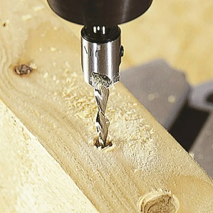 Wolfcraft Broca para madera con avellanador 3,5 - 9,5 mm - 1 ud., Diámetro de la broca: 150 mm - Se está utilizando una broca avellanadora para perforar un agujero en un trozo de madera. La broca está conectada a un taladro y la madera está cubierta de serrín.