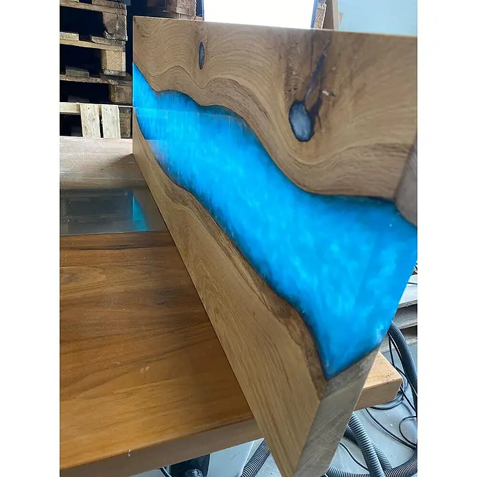 CreativEpoxy Gießharz Resin 50 A+B - 6,75 kg, Passend für: Bis zu 50 mm Schichtstärke - Detailansicht eines dekorativen Holztisches mit eingelassenem, leuchtend blauem Epoxidharz, das einen faszinierenden Fluss-Effekt erzeugt.
