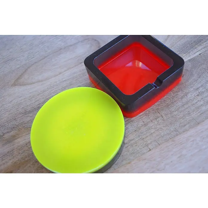 CreativEpoxy Gießharz Resin 20 A+B - 850 g, Passend für: Bis zu 20 mm Schichtstärke - Nahaufnahme von einem schwarzen und roten quadratischen Aschenbecher und einem runden gelben Deckel auf einem Holztisch.