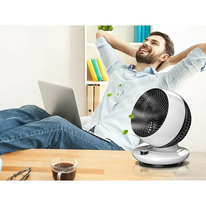 Purline Venty Ventilador de sobremesa TA 45 - Blanco y Negro, 27 cm - Imagen de un ventilador blanco con corrientes de aire, colocado sobre una mesa frente a un hombre relajado.