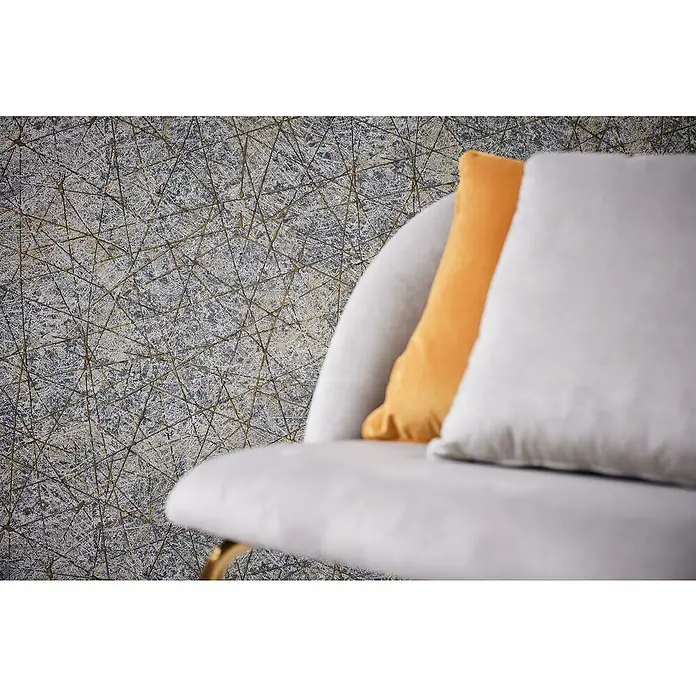 A.S. Création Metropolitan Stories Travel Styles Vliestapete Allover II - Schwarz/Gold, Grafisch, 10,05 x 0,53 m - Nahaufnahme eines Sessels mit einem grauen und einem orangefarbenen Kissen vor einer Wand mit geometrischem Muster. Elegantes Interieur.