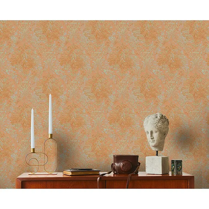 A.S. Création Metropolitan Stories Travel Styles Vliestapete Damask - Orange, Ornament, 10,05 x 0,53 m - Dekorative Stillleben-Komposition mit antiker Büste, Kerzen und Vintage-Kamera auf einem Sideboard vor gemusterter Tapete.