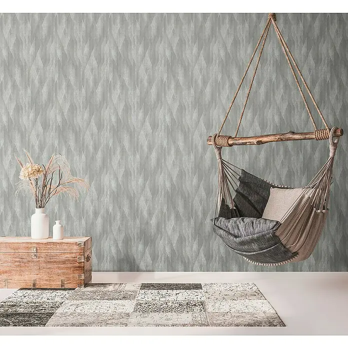 A.S. Création Metropolitan Stories Travel Styles Vliestapete Vintage - Dunkelgrau, Grafisch, 10,05 x 0,53 m - Elegante Hängehöhle mit Kissen und Überwurf, die Gemütlichkeit verspricht, vor einer dezent gemusterten Wand und einem passenden Teppich.