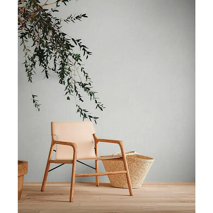 A.S. Création Metropolitan Stories Travel Styles VliestapeteHellgrau, Uni, 10,05 x 0,53 m, Feine Struktur - Elegantes Interieur mit einem hellen Holzstuhl mit Lederakzenten und einem Weidenkorb, hervorgehoben durch einen grünen Zweig.