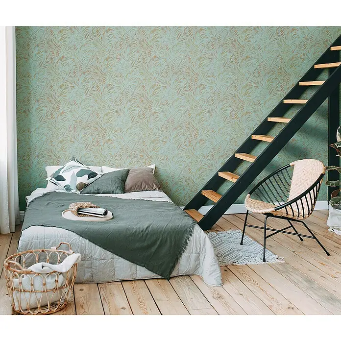 A.S. Création Metropolitan Stories Travel Styles Vliestapete Blätter-Allover I - Türkis, Floral, 10,05 x 0,53 m - Schlafzimmer mit Bett, Leiter und Rattansessel. Die Wand ist mit einem Blattmuster tapeziert, das eine gemütliche Atmosphäre schafft.