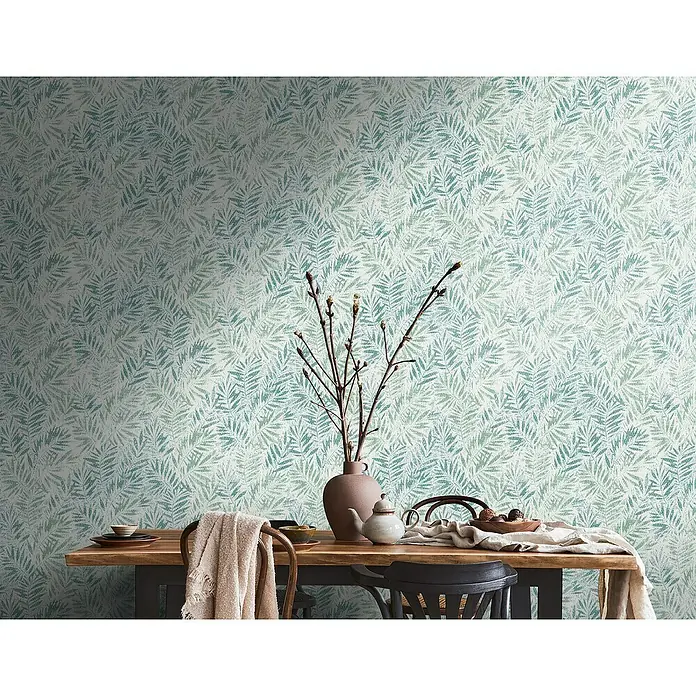 A.S. Création Metropolitan Stories Travel Styles Vliestapete Blätter-Allover IGrün, Floral, 10,05 x 0,53 m - Ein Tisch mit Geschirr, einer Vase und einem Tuch vor einer Wand mit einem floralen Muster. Gemütliches Ambiente für Mahlzeiten.
