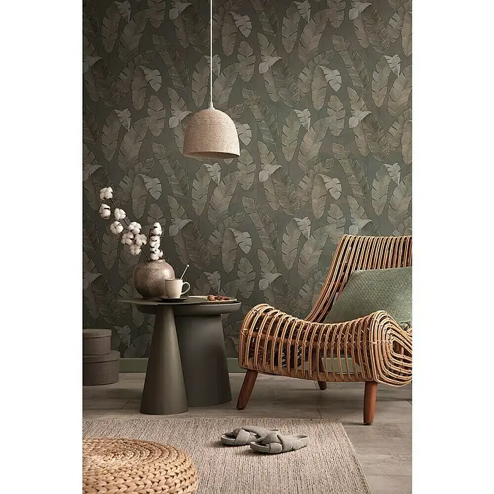 A.S. Création Metropolitan Stories Travel Styles Vliestapete - Braun, Floral, 10,05 x 0,53 m - Nahaufnahme eines stilvollen Wohnzimmers mit Rattan-Sessel, Beistelltisch und einer dekorativen Hängelampe, die eine gemütliche Atmosphäre schaffen.