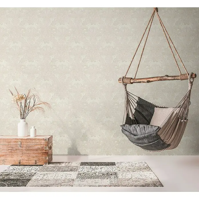 A.S. Création Metropolitan Stories Travel Styles Vliestapete DamaskCreme, Ornament, 10,05 x 0,53 m - Einladender Innenraum mit einer stilvollen Hänge-Hängematte mit Kissen, über einem Patchwork-Teppich, neben einem Vintage-Holztruhe mit dekorativer Vase.