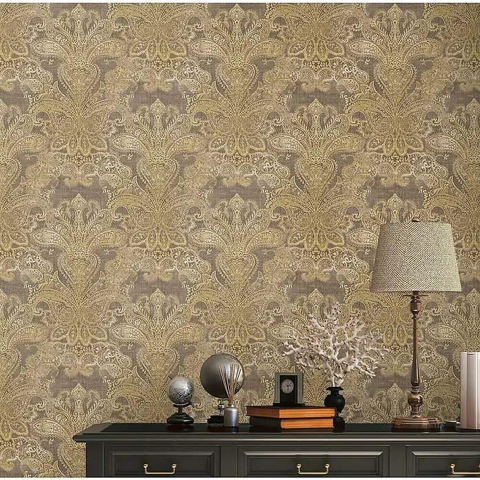 A.S. Création Metropolitan Stories Travel Styles Vliestapete DamaskGold/Braun, Ornament, 10,05 x 0,53 m - Nahaufnahme eines Tisches mit Globus, Lampe und Büchern vor einer Wand mit dekorativem, goldenem Paisley-Muster.
